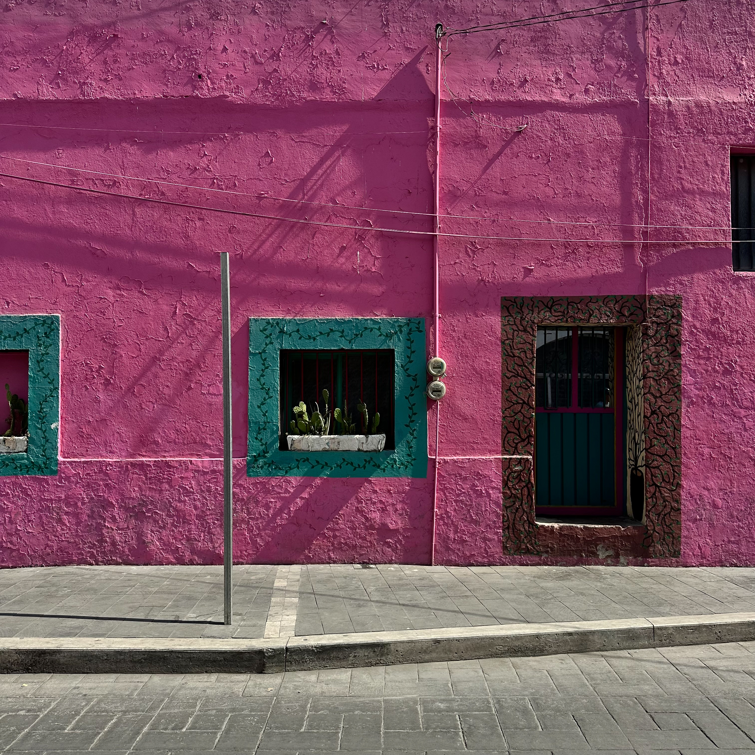 Bright pink Mexican street wall with teal window frames and door